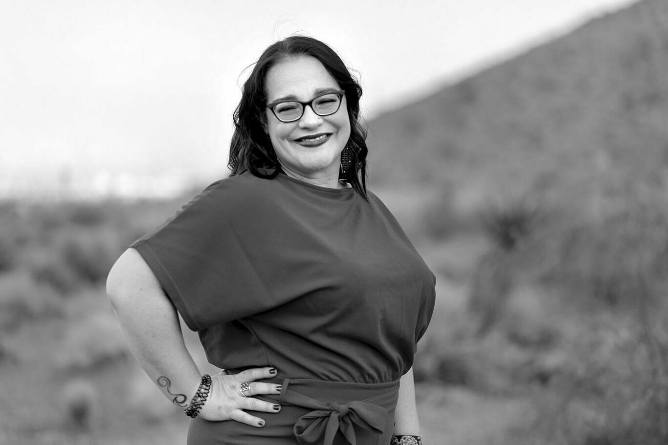 Stacey is standing in the desert, smiling. Picture is in black and white