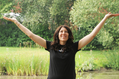 Picture of Rebecca Bishop  with her arms in the air with a big smile with a background of trees